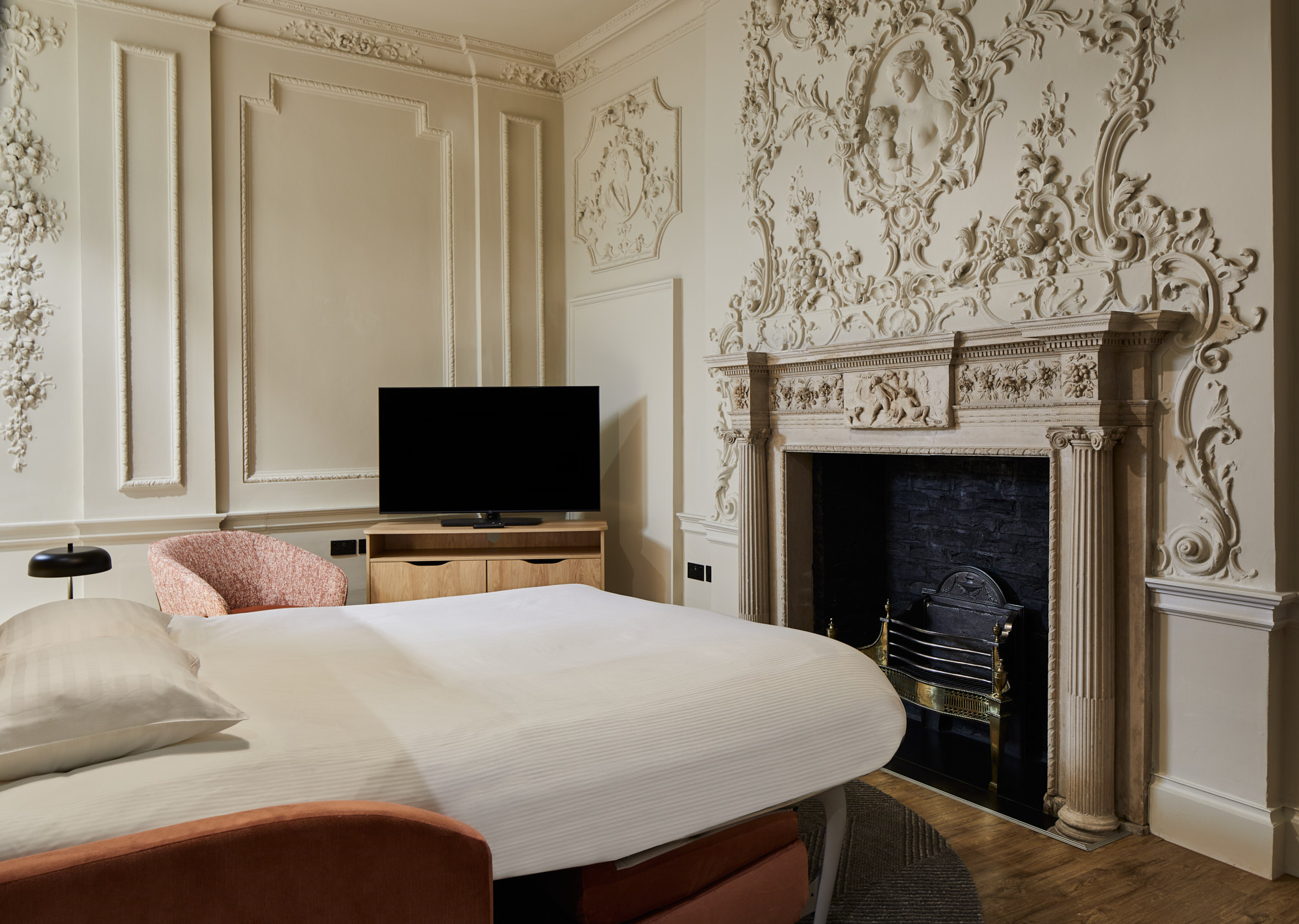 Living area with decorative fireplace, TV, and pink sofa, blending historic architecture with contemporary furnishings.