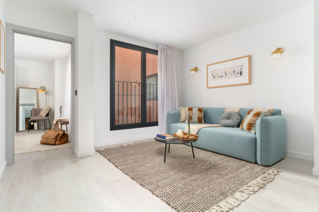 Lightwell Apartment at master La Rambla – bright living room with pastel blue sofa, textured rug, and view into the cozy bedroom.