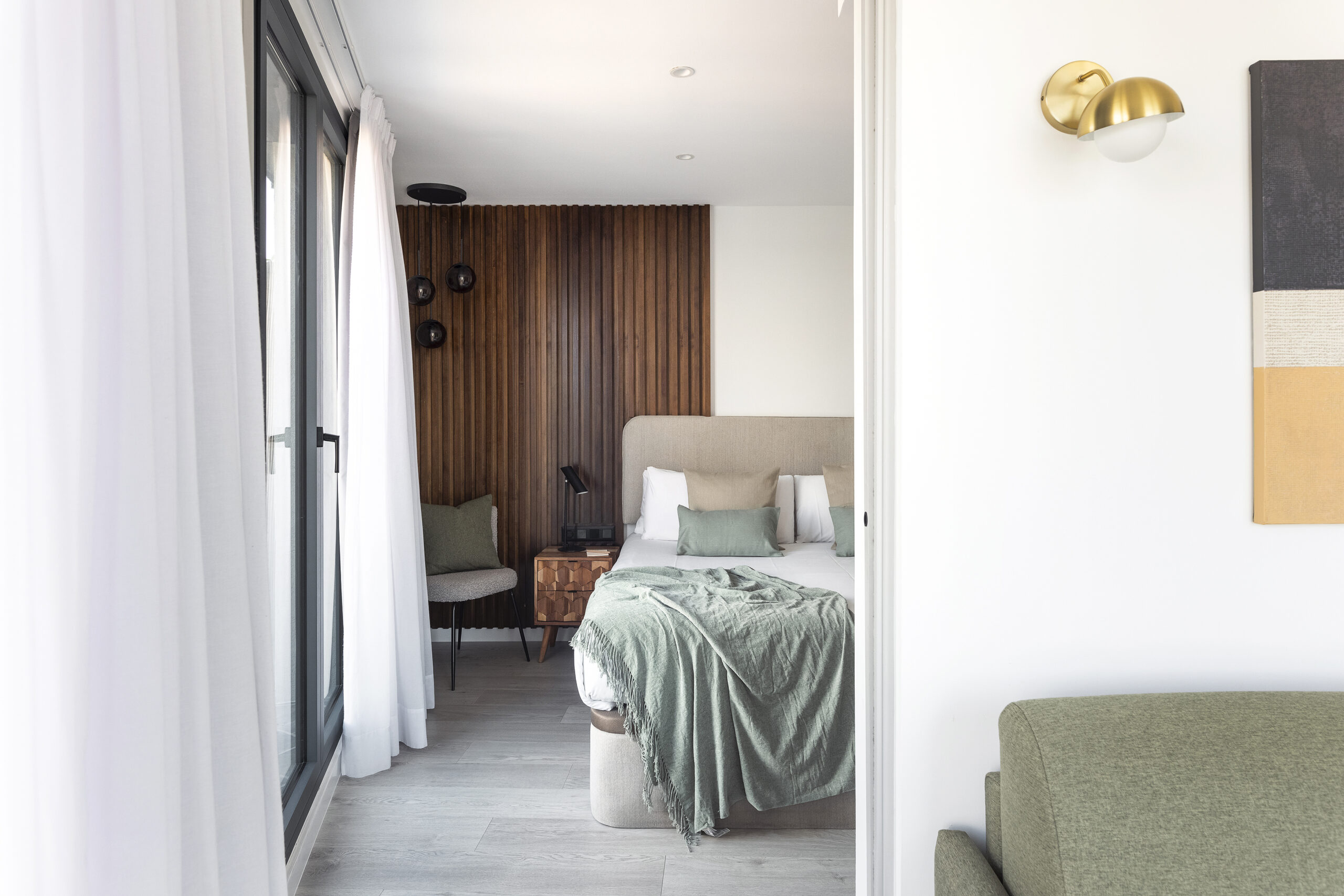Stylish bedroom at master La Rambla Barcelona with soft-toned bedding, wood-paneled accent wall, and private balcony access.