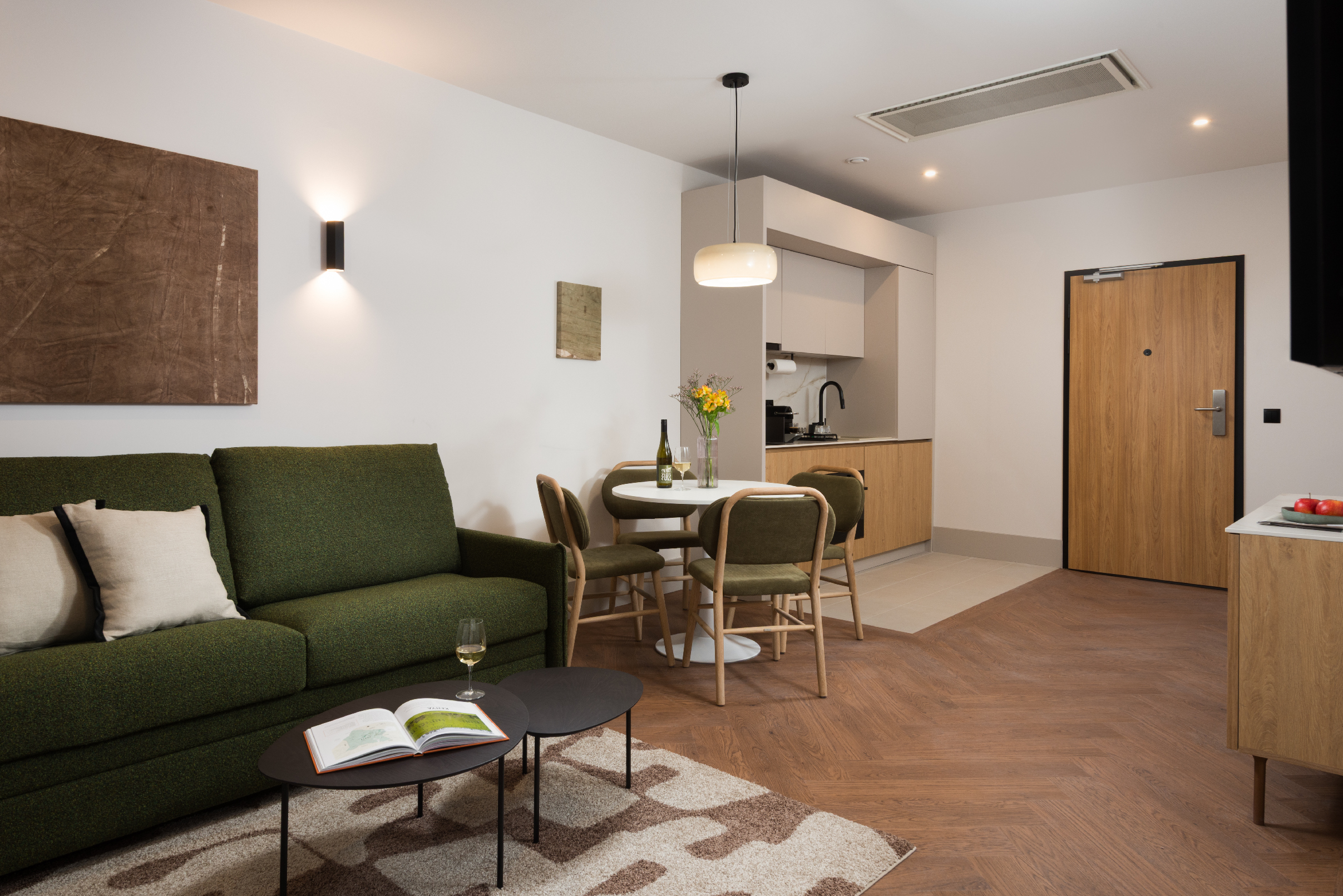 Living area of the Family Apartment at master Wola Warsaw with green sofa, coffee table, soft lighting, and large window with curtains.