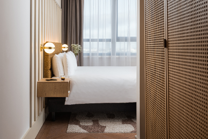 Two bedroom apartment at master Wola featuring a comfortable double bed, warm lighting, and modern wood-accented design.