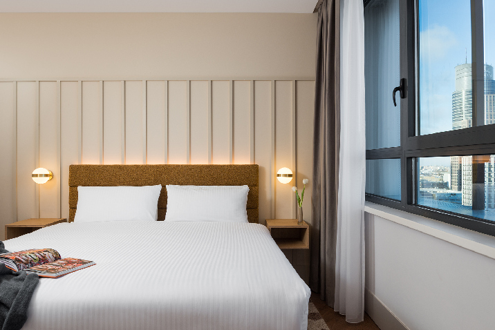 Main bedroom in master Wola two bedroom apartment with double bed, soft neutral tones, and large window overlooking Warsaw