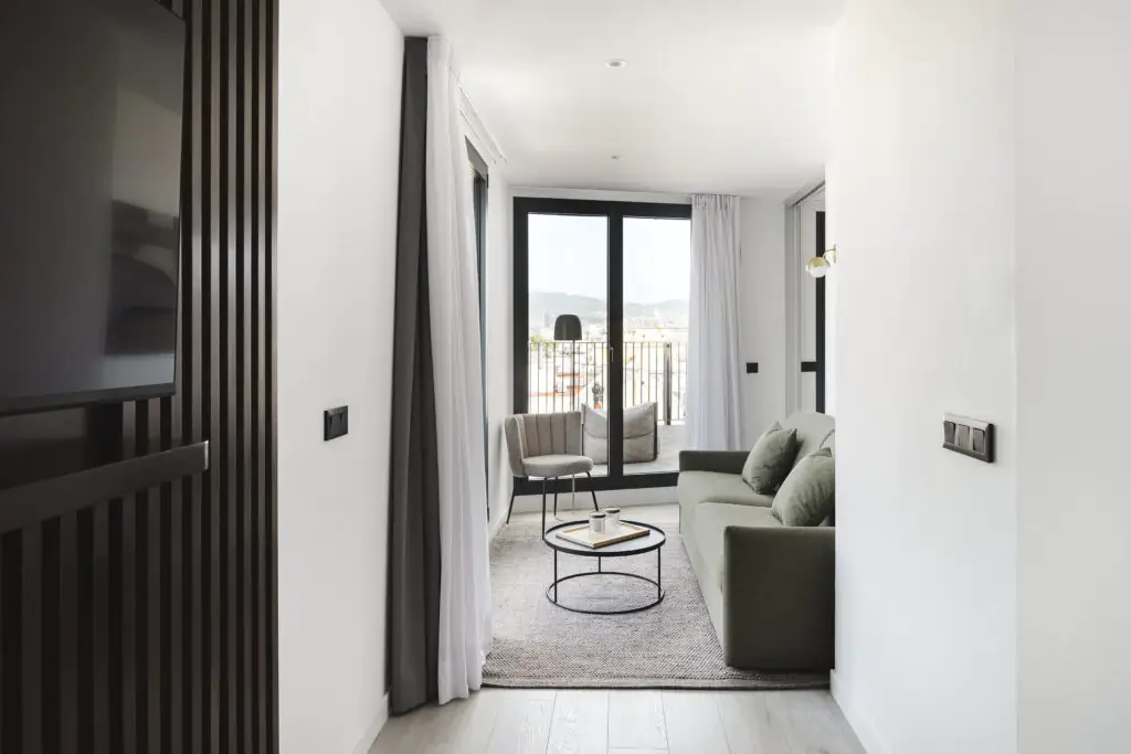 Bright living room at master La Rambla Barcelona with green sofa, round coffee table, and access to a spacious terrace with city views.