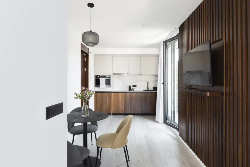 Modern open-plan kitchen and dining space at master La Rambla Barcelona featuring wood finishes, marble backsplash, and flat-screen TV.