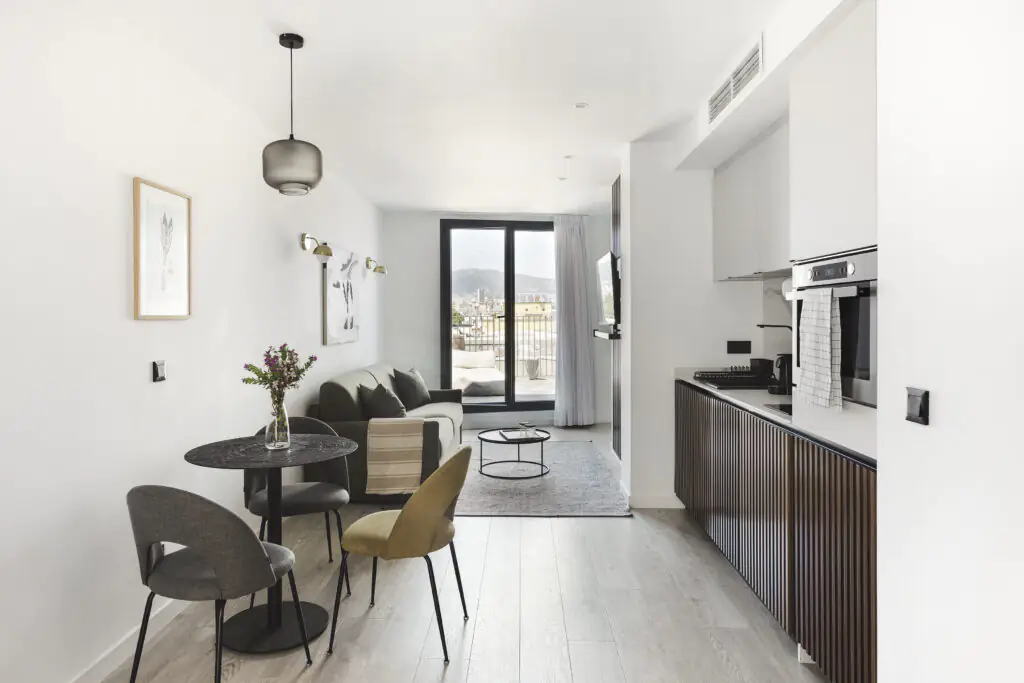 Spacious living room at master La Rambla Barcelona with sofa, dining table, fully equipped kitchen, and balcony doors with city views.