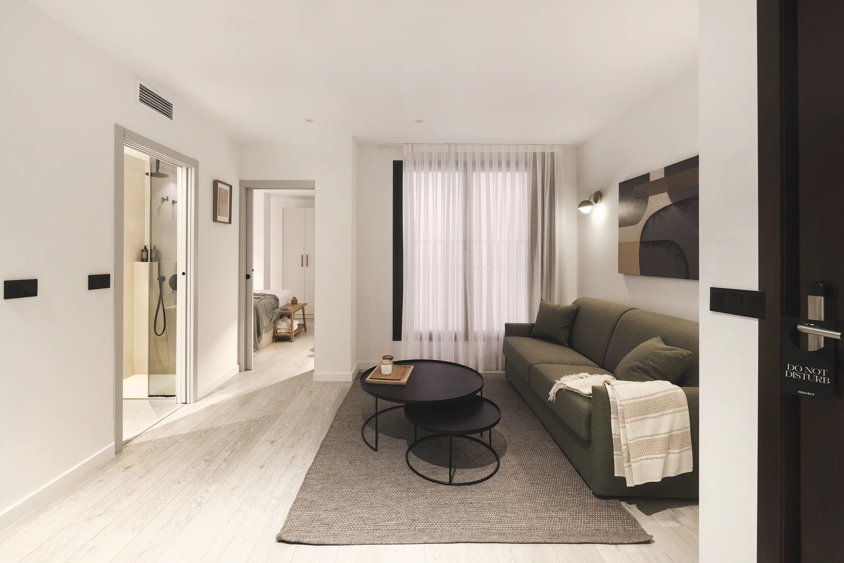 Cozy living room at master La Rambla Barcelona with green sofa, coffee tables, and view into the bedroom and bathroom.