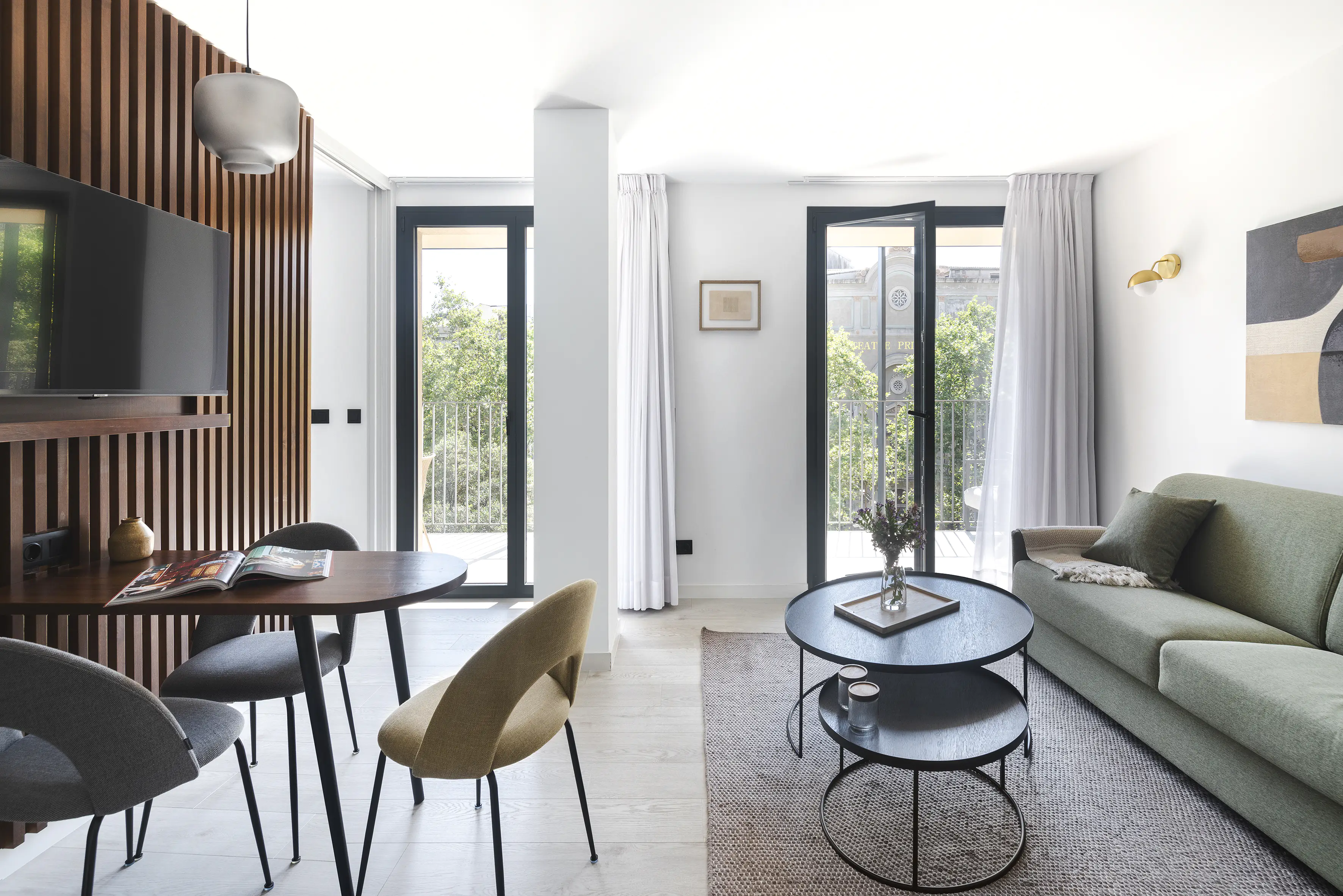 Modern living room at master La Rambla Barcelona with green sofa, dining table, and balcony doors bringing in natural light.