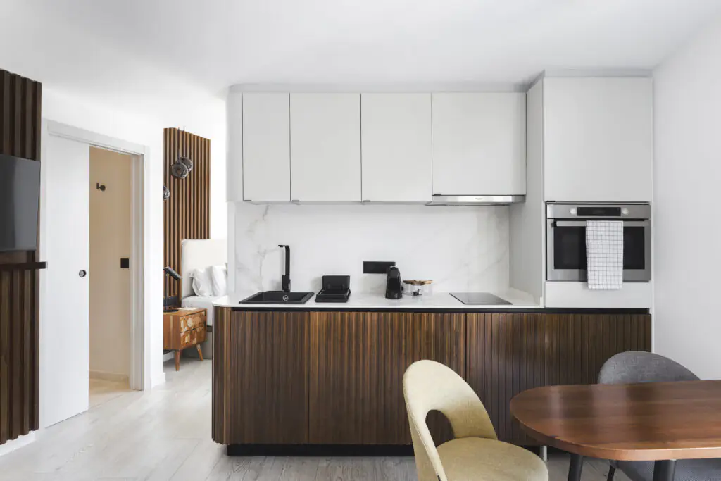Stylish kitchen at master La Rambla Barcelona with wood-panel cabinets, marble backsplash, black sink, oven, and dining table.