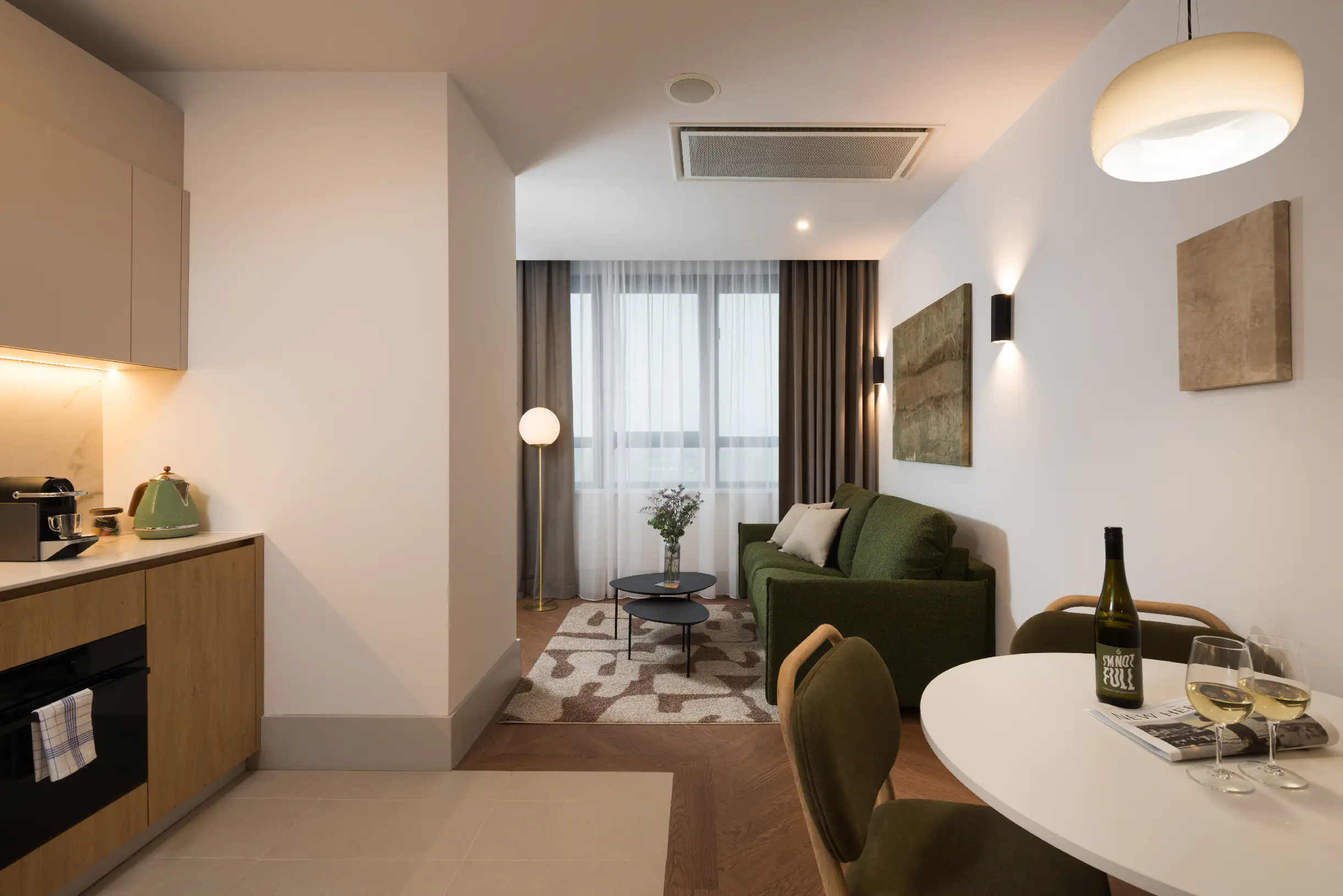 Open-plan living area at master Wola Serviced Apartments with kitchenette, dining table, and green sofa seating area