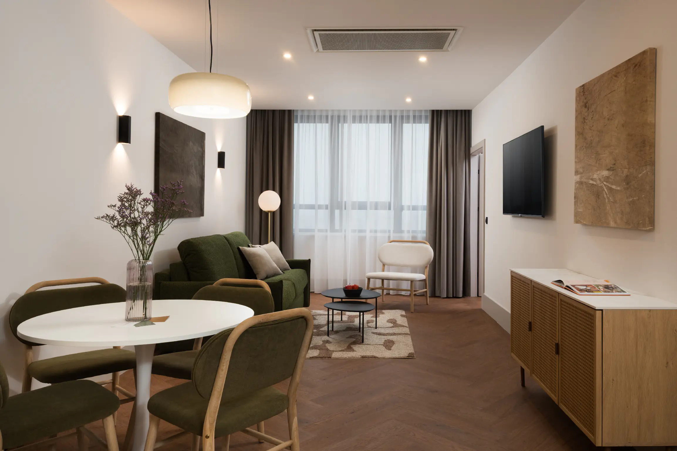 Modern living and dining area at master Wola Serviced Apartments with green sofa, round dining table, and soft natural light