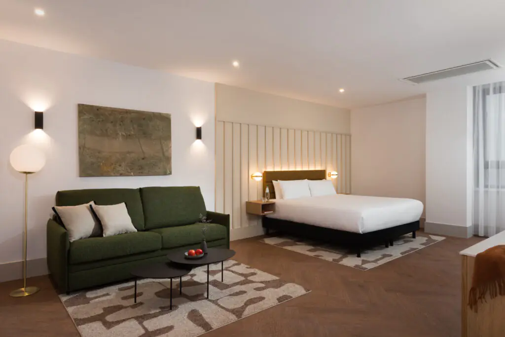 Spacious studio apartment at master Wola Serviced Apartments with double bed, green sofa, and seating area